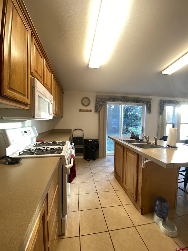 kitchen with sink, a textured ceiling, light tile patterned floors, a kitchen breakfast bar, and white appliances