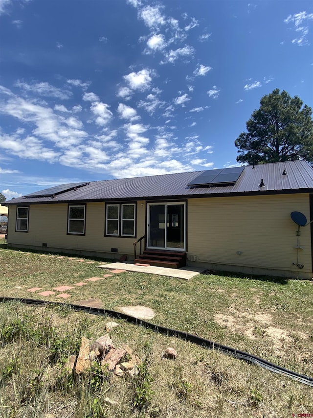 rear view of property featuring a yard and solar panels