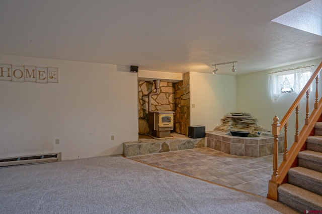 carpeted living room with a wood stove, baseboard heating, rail lighting, and a textured ceiling