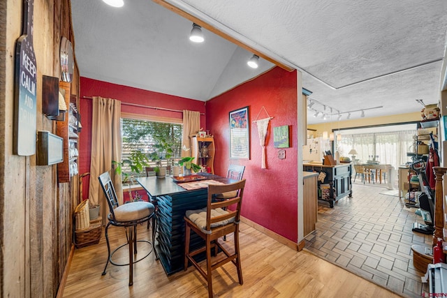 dining area featuring track lighting, vaulted ceiling, light wood-type flooring, and a textured ceiling