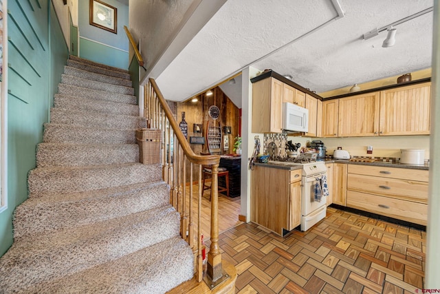 kitchen featuring a textured ceiling, white appliances, light brown cabinetry, and parquet floors