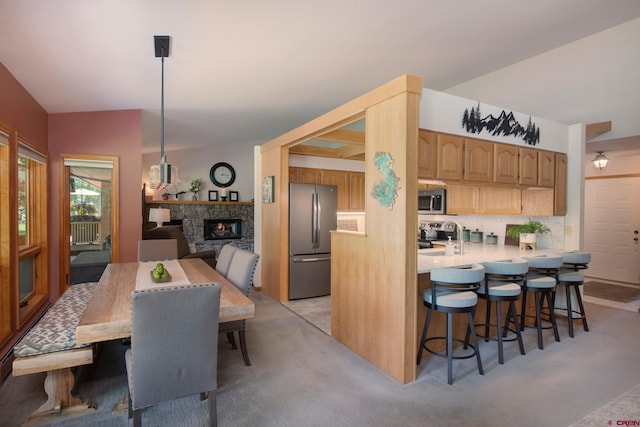 kitchen with stainless steel appliances, a stone fireplace, light countertops, decorative backsplash, and a kitchen breakfast bar