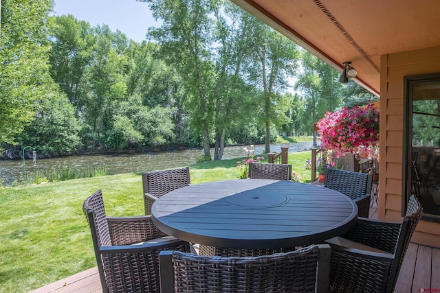 deck with outdoor dining space, a yard, and a water view