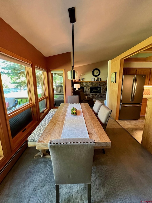 dining area featuring a stone fireplace, lofted ceiling, dark colored carpet, and baseboard heating