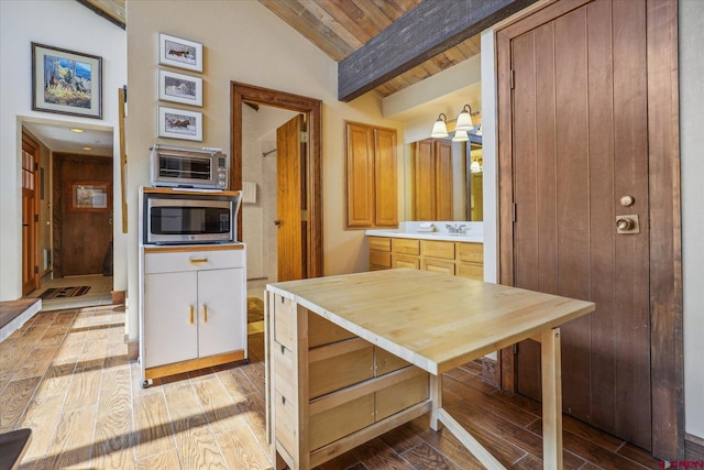 kitchen featuring stainless steel microwave, vaulted ceiling with beams, white cabinets, hardwood / wood-style flooring, and sink