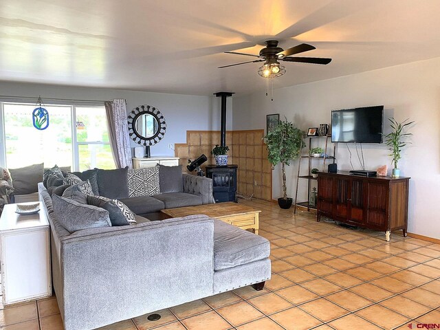 tiled living room featuring a wood stove and ceiling fan