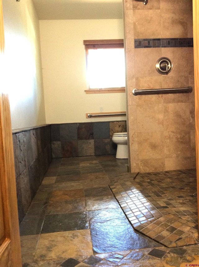 bathroom with toilet, stone finish flooring, and a tile shower