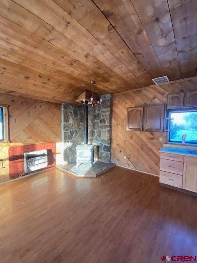 bonus room with wooden walls, wood finished floors, wood ceiling, visible vents, and a wood stove