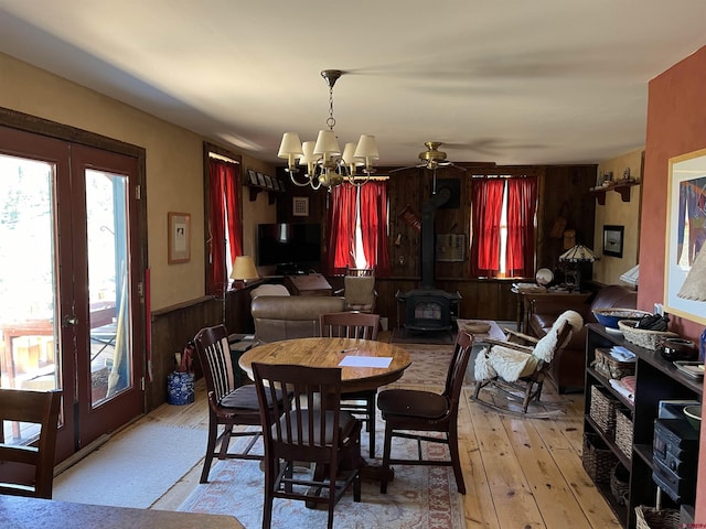 dining room with a wood stove, light hardwood / wood-style floors, french doors, a chandelier, and wood walls