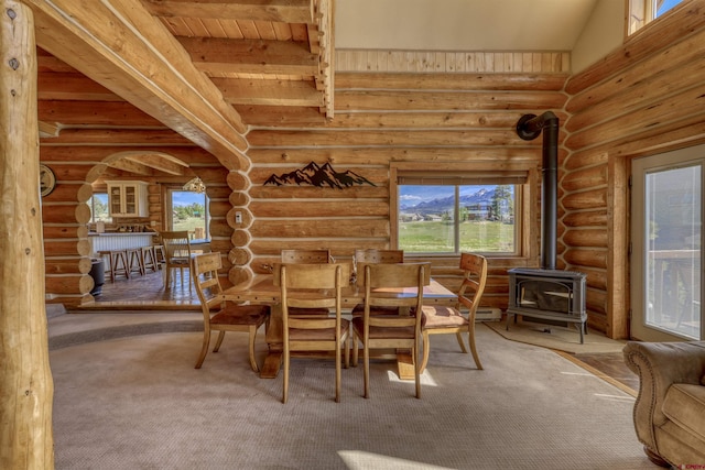 carpeted dining space with beamed ceiling, wooden ceiling, a wood stove, and log walls