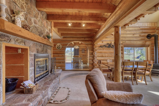 living room with a stone fireplace, rustic walls, wood ceiling, carpet flooring, and beamed ceiling