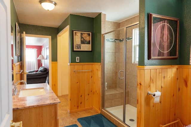 full bathroom featuring a shower stall, wooden walls, vanity, and wainscoting