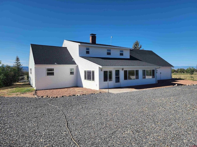 rear view of property featuring a patio area, a chimney, and roof with shingles