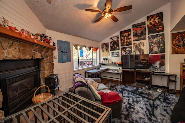 interior space featuring vaulted ceiling, a stone fireplace, wood walls, ceiling fan, and a textured ceiling