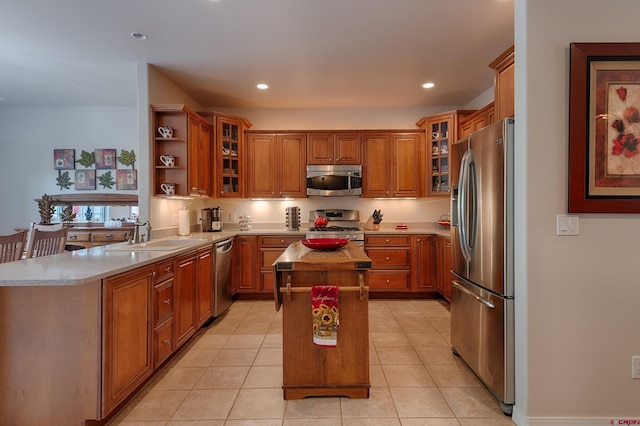 kitchen with light stone counters, stainless steel appliances, sink, light tile patterned floors, and a kitchen island