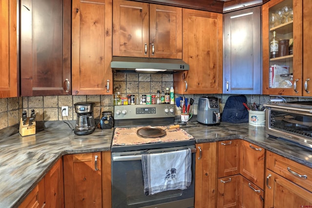 kitchen featuring under cabinet range hood, stainless steel electric range, glass insert cabinets, and brown cabinetry