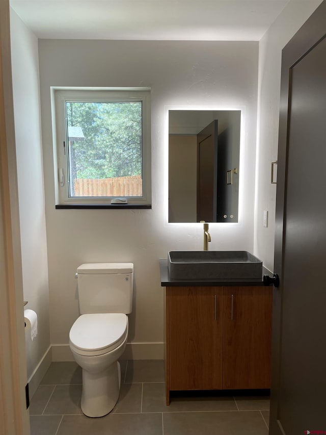 half bath featuring toilet, tile patterned flooring, vanity, and baseboards