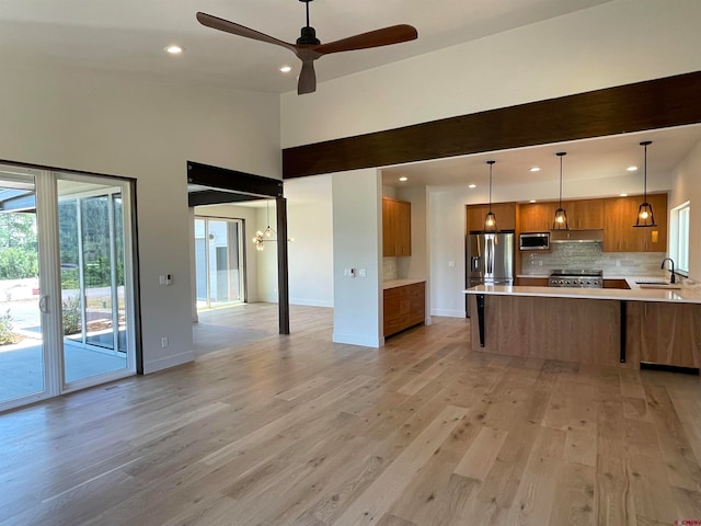 kitchen with appliances with stainless steel finishes, light hardwood / wood-style flooring, sink, pendant lighting, and backsplash