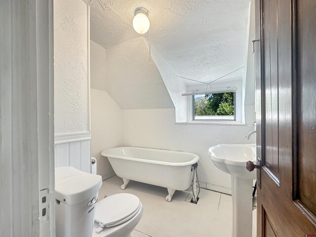 bathroom with a textured ceiling, a tub, toilet, lofted ceiling, and tile patterned flooring