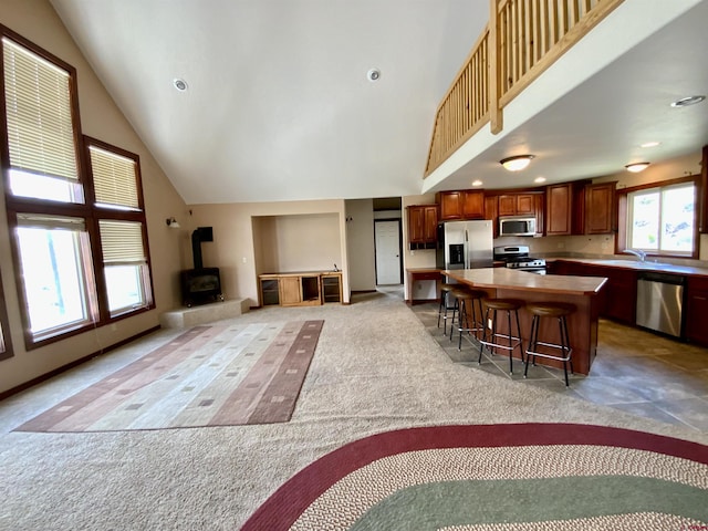 kitchen featuring a wood stove, stainless steel appliances, high vaulted ceiling, a breakfast bar area, and a kitchen island