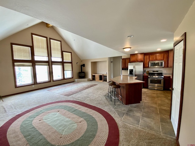 kitchen featuring a wood stove, a center island, a kitchen breakfast bar, dark carpet, and appliances with stainless steel finishes