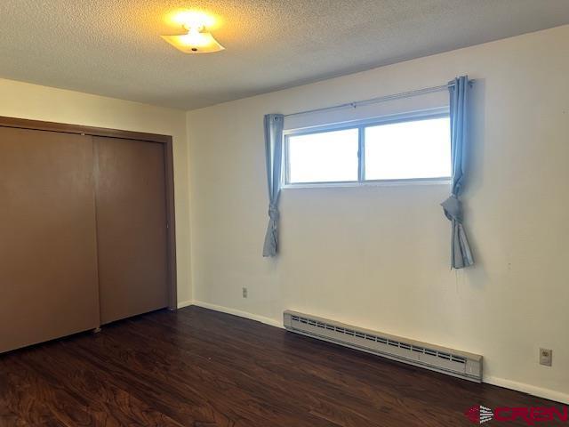 unfurnished bedroom with dark hardwood / wood-style flooring, a textured ceiling, a closet, and a baseboard heating unit