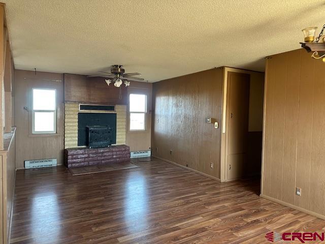 unfurnished living room featuring wooden walls, a healthy amount of sunlight, a textured ceiling, and hardwood / wood-style flooring