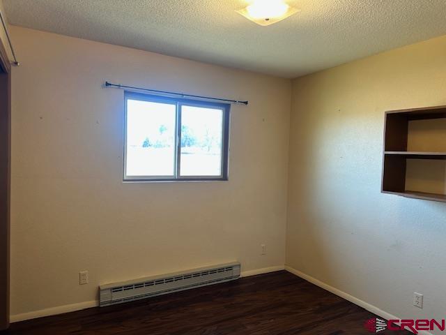 empty room featuring a textured ceiling, dark wood-type flooring, and a baseboard radiator