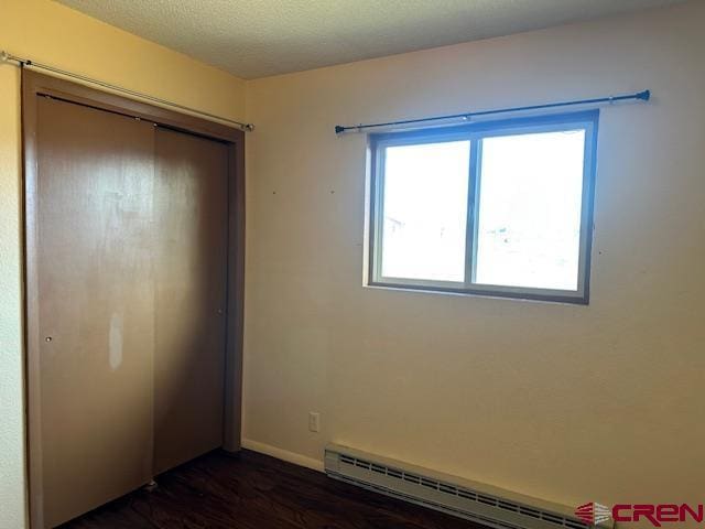 unfurnished bedroom with dark wood-type flooring, a closet, and a baseboard radiator