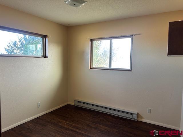 empty room with a textured ceiling, plenty of natural light, dark wood-type flooring, and a baseboard radiator