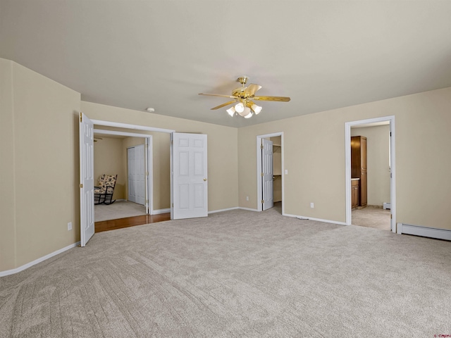 unfurnished bedroom with connected bathroom, a walk in closet, ceiling fan, baseboard heating, and light carpet