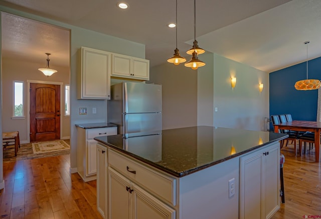 kitchen featuring decorative light fixtures, white cabinets, dark stone countertops, stainless steel fridge, and a kitchen island