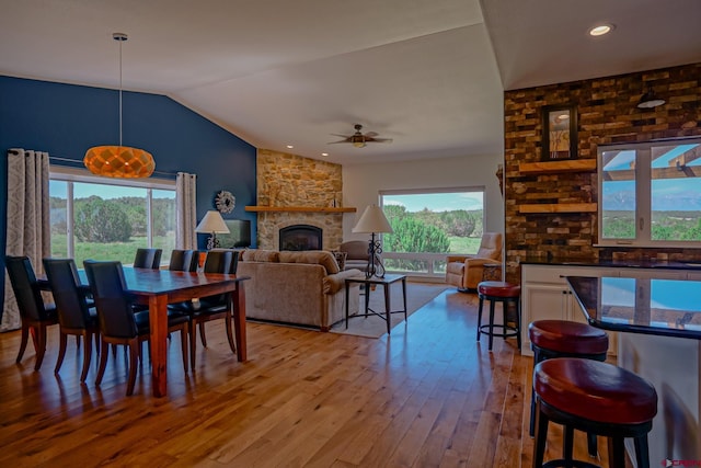 dining space featuring a fireplace, ceiling fan, vaulted ceiling, and light wood-type flooring