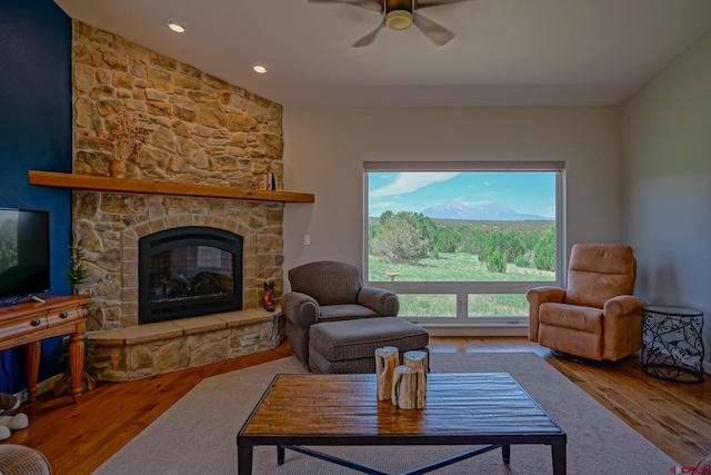 living room with wood-type flooring, ceiling fan, a healthy amount of sunlight, and a stone fireplace