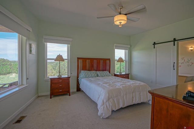 bedroom with multiple windows, ceiling fan, light carpet, and a barn door