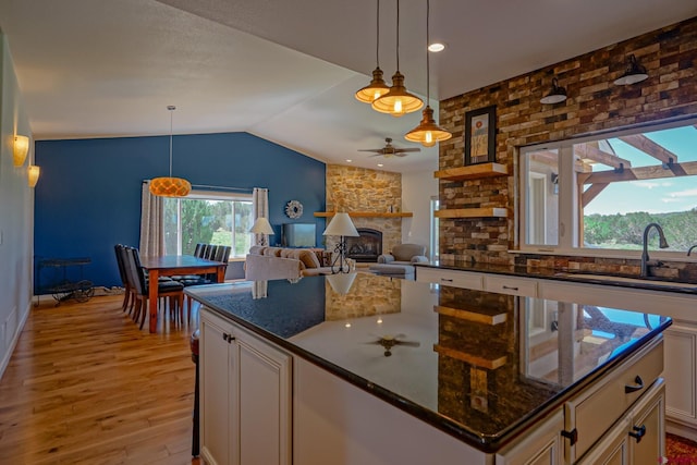 kitchen with sink, decorative light fixtures, white cabinets, dark stone counters, and a stone fireplace