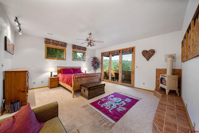 carpeted bedroom featuring ceiling fan, access to outside, rail lighting, and a wood stove