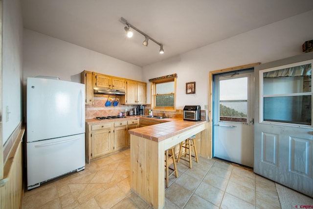 kitchen featuring decorative backsplash, white fridge, tile countertops, and light brown cabinets