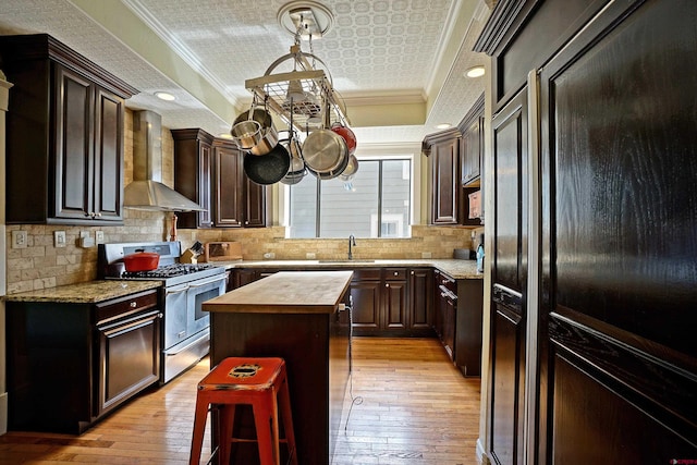 kitchen with wall chimney range hood, ornamental molding, a kitchen island, and range with two ovens