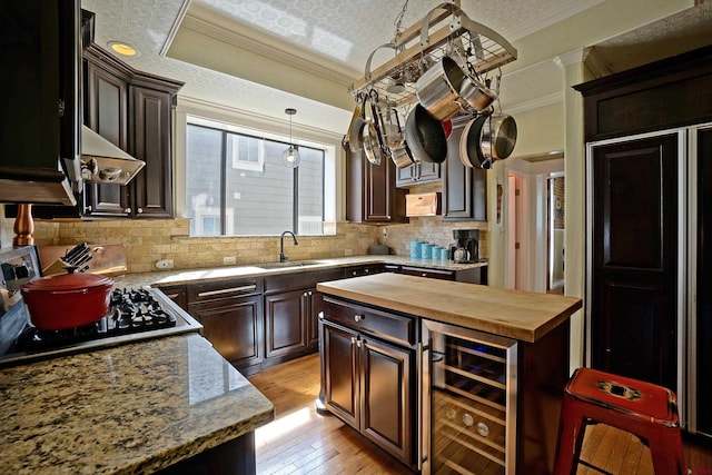 kitchen with wooden counters, sink, crown molding, light wood-type flooring, and beverage cooler