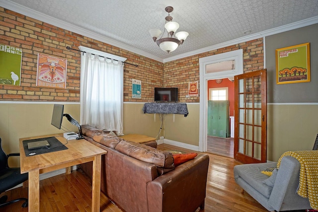 living room with light wood-type flooring, brick wall, a chandelier, and crown molding