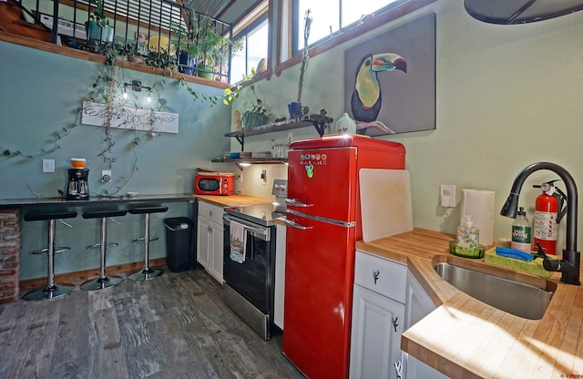 kitchen with white cabinets, butcher block countertops, stainless steel electric range oven, and dark hardwood / wood-style flooring