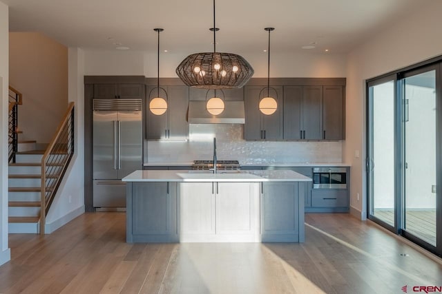 kitchen with decorative light fixtures, light hardwood / wood-style flooring, stainless steel appliances, and a center island with sink