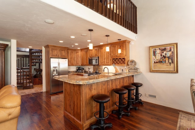 kitchen with stainless steel appliances, kitchen peninsula, hanging light fixtures, light stone countertops, and dark wood-type flooring