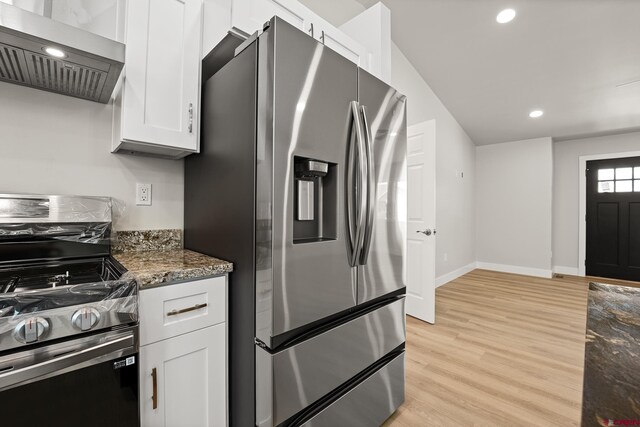 kitchen featuring white cabinetry, wall chimney range hood, dark stone countertops, light hardwood / wood-style floors, and appliances with stainless steel finishes