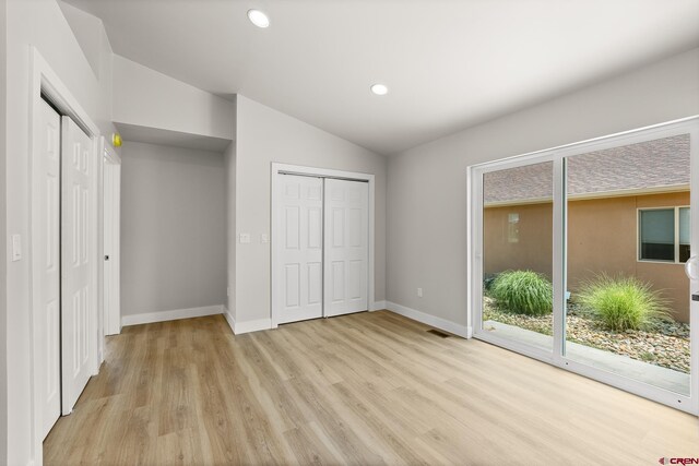 unfurnished bedroom featuring vaulted ceiling, light hardwood / wood-style flooring, and access to exterior