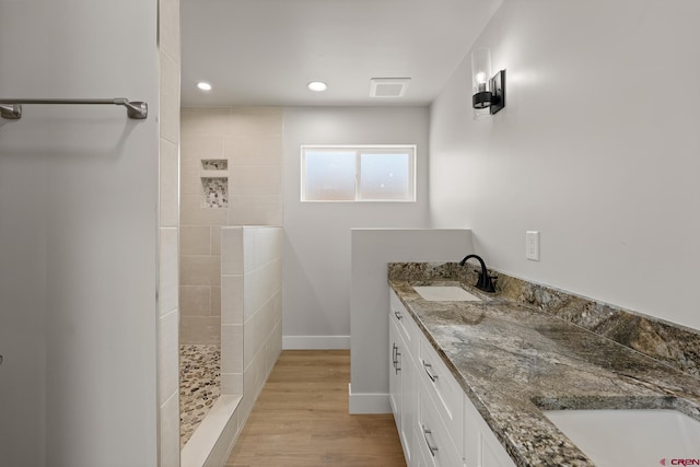 bathroom featuring wood-type flooring, double sink vanity, and a tile shower