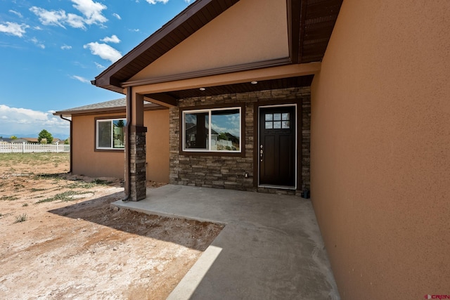 property entrance with stone siding, a patio area, fence, and stucco siding