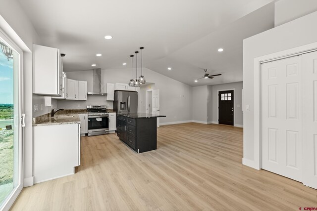 kitchen featuring wall chimney range hood, stainless steel appliances, dark stone countertops, vaulted ceiling, and light hardwood / wood-style flooring