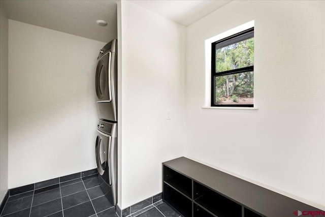 laundry room with stacked washer and dryer and dark tile patterned flooring